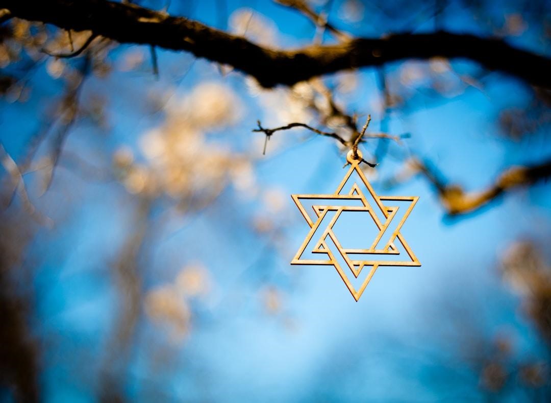 A beautiful carved wood Star of David ornament hangs from a tree outdoors.