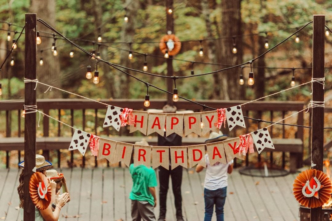 A few people talk on a deck with a "Happy Birthday" sign hung above them.