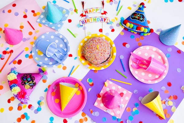 An assortment of colorful party supplies like paper plates, hats, and a cake sitting on a table.