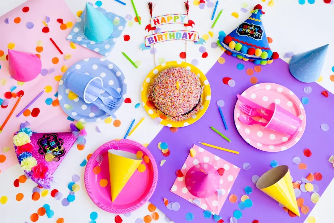 "Happy Birthday" party table with bright pink, purple and blue plates, party hats and confetti.