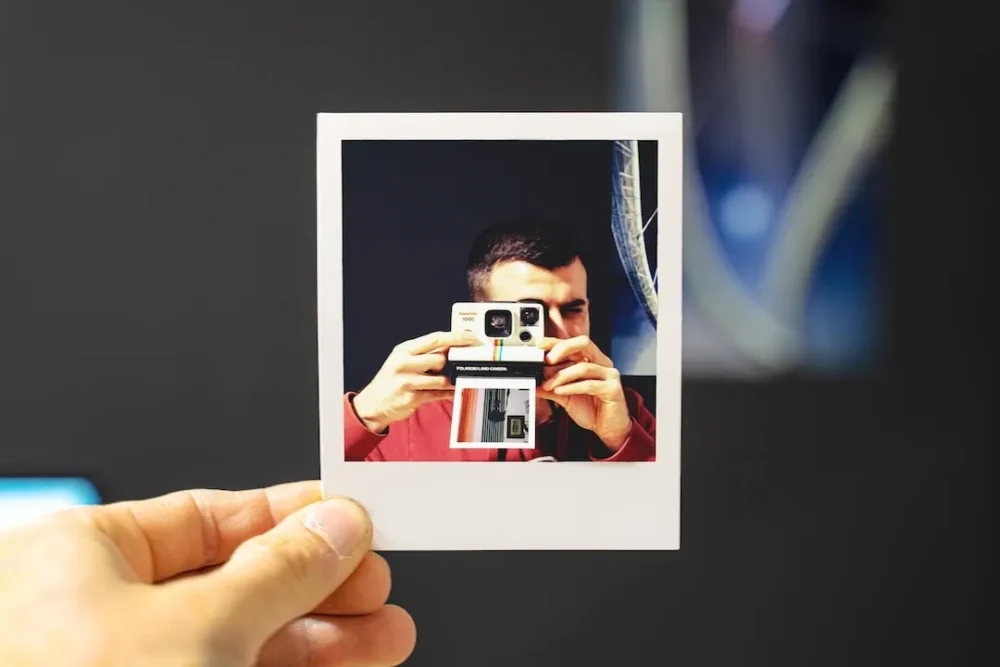 Hand holding a polaroid of a man taking a polaroid.
