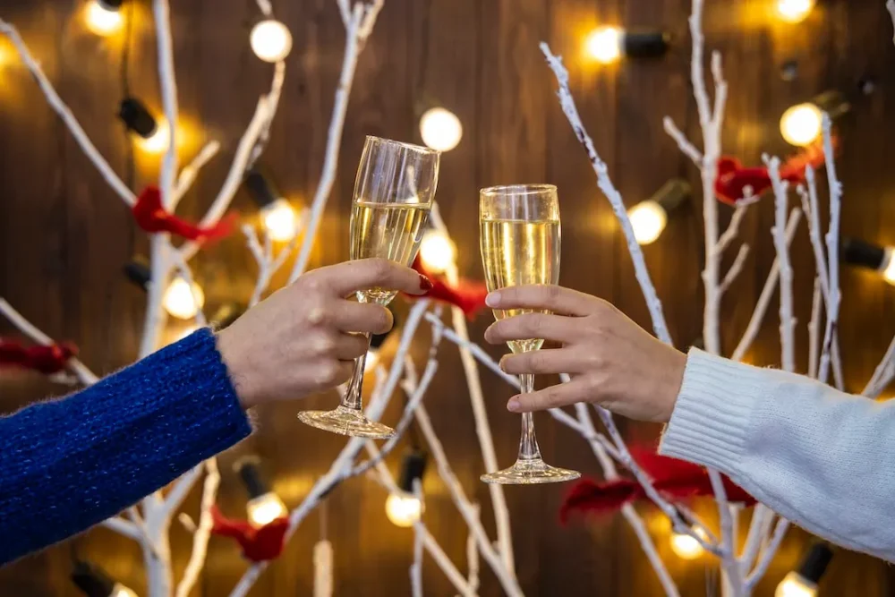 Two party guests clink glasses in front of a Christmas display.