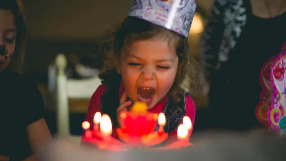 An excited young girl blows out candles on a birthday cake.